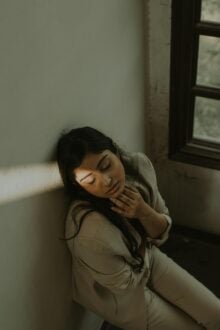 A woman sits near a window, a beam of light shining on one side of her face