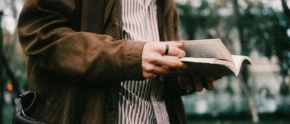 A man stands holding a book in his hand, engaged in reading or contemplating its contents.