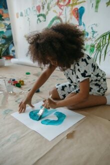 A young girl joyfully paints on paper with a brush, showcasing her creativity and artistic expression.