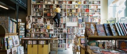 A person using a ladder to access books in a charming bookstore, surrounded by rows of colorful book spines.