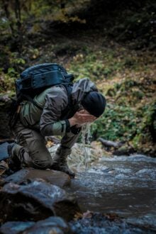 A man is refreshing himself by washing his face in a gentle stream, immersed in the beauty of the outdoors.