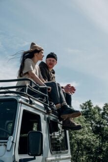 Two people seated on the roof of a parked car