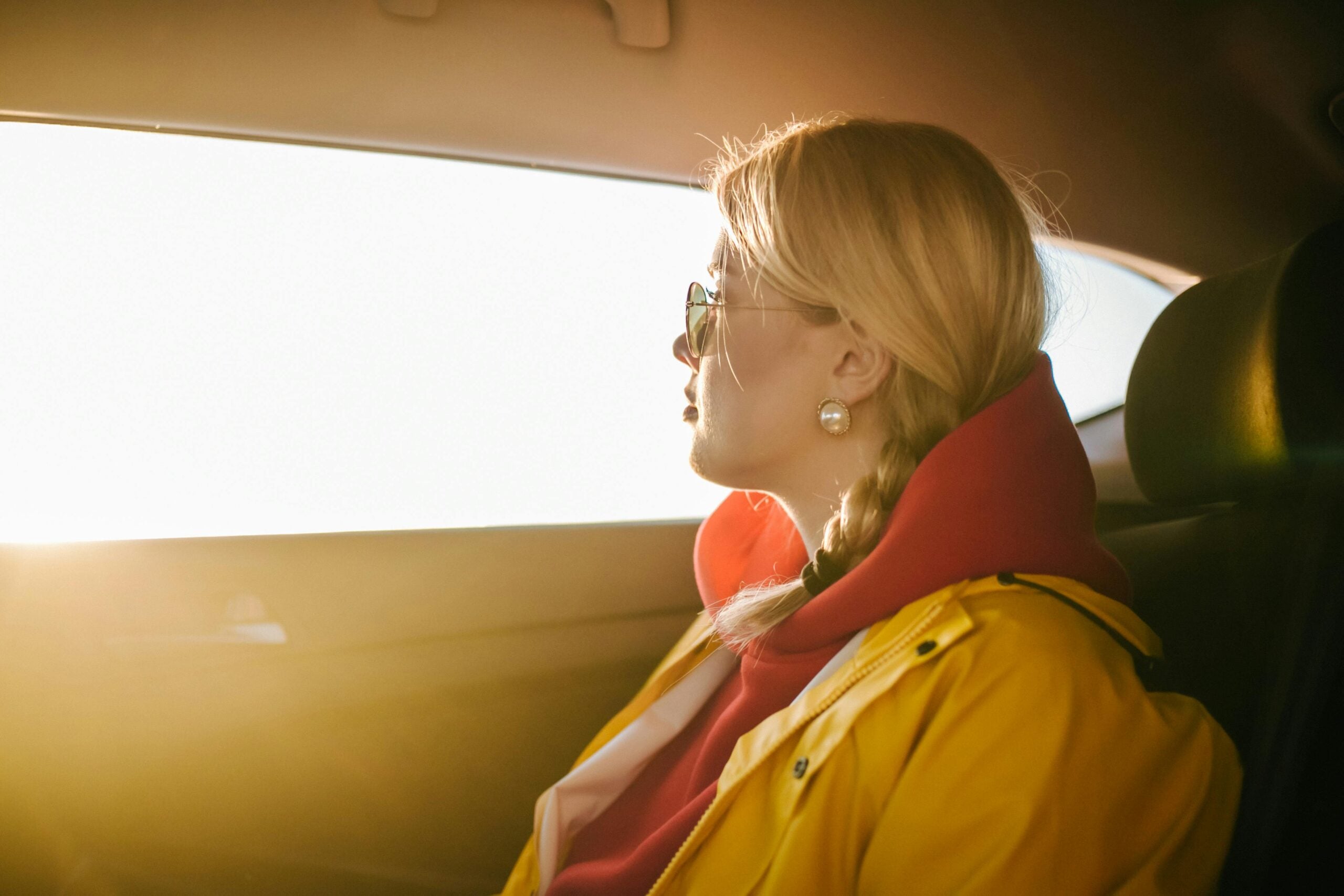 A person wearing sunglasses looks out a brightly lit car window