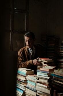 A person stands in a dim room surrounded by stacks and stacks of paperback books several feet high