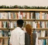 Two people stand side by side, their backs to the camera, perusing well-stocked bookshelves