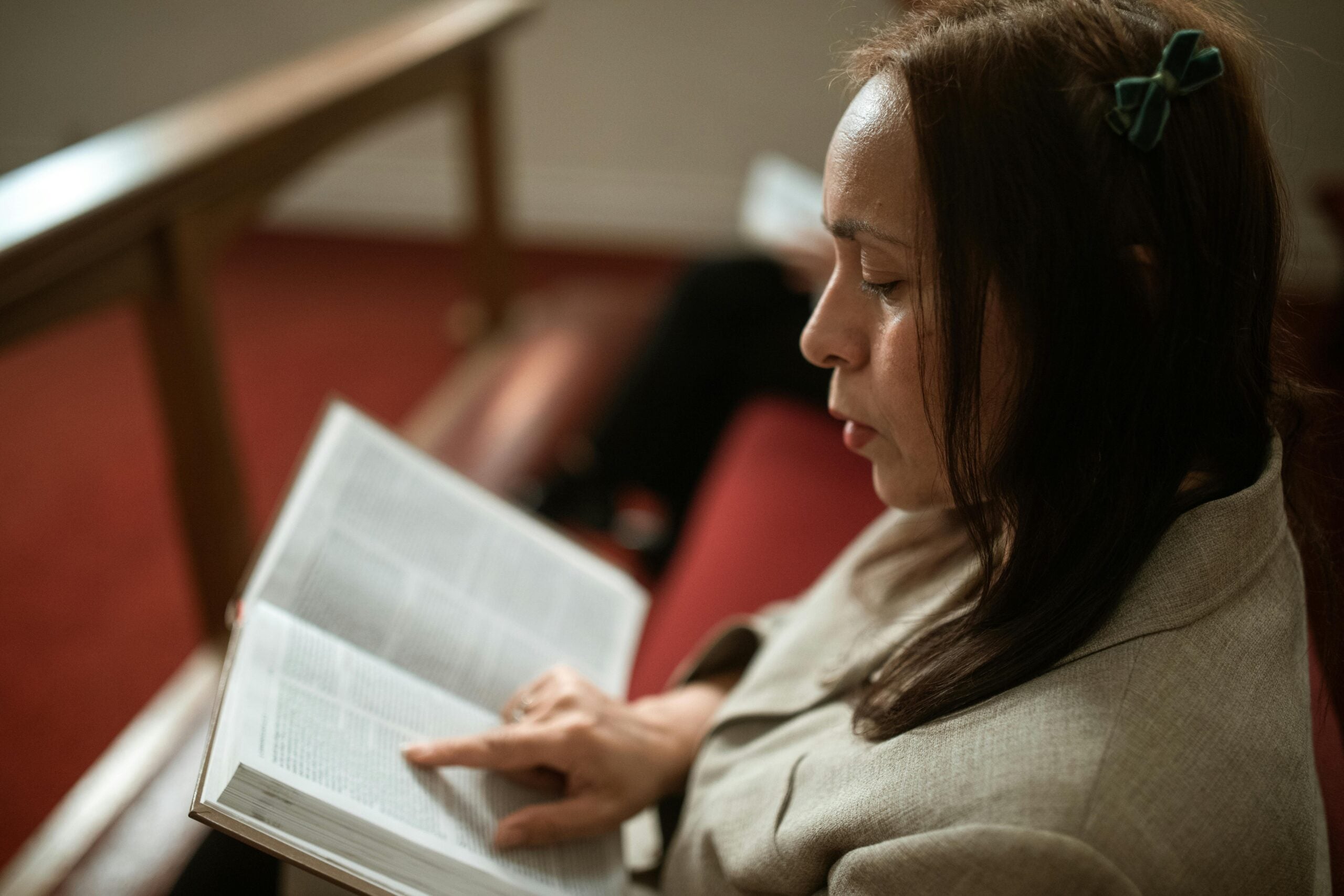 A person sits in a pew, their finger scanning the text in a holy book