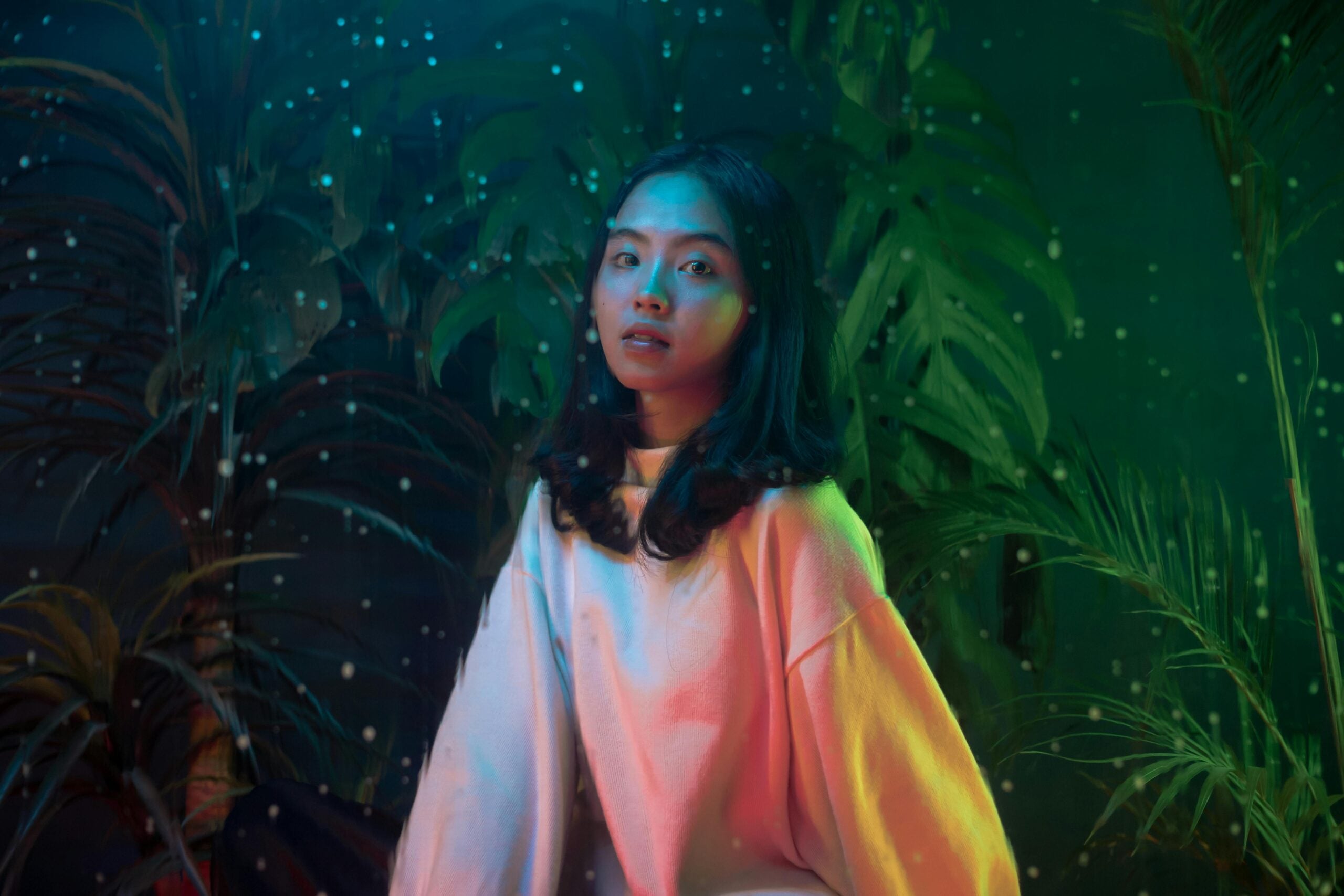 A person sits in a verdant, wooded setting, surrounded by small orbs and bathed in otherworldly light